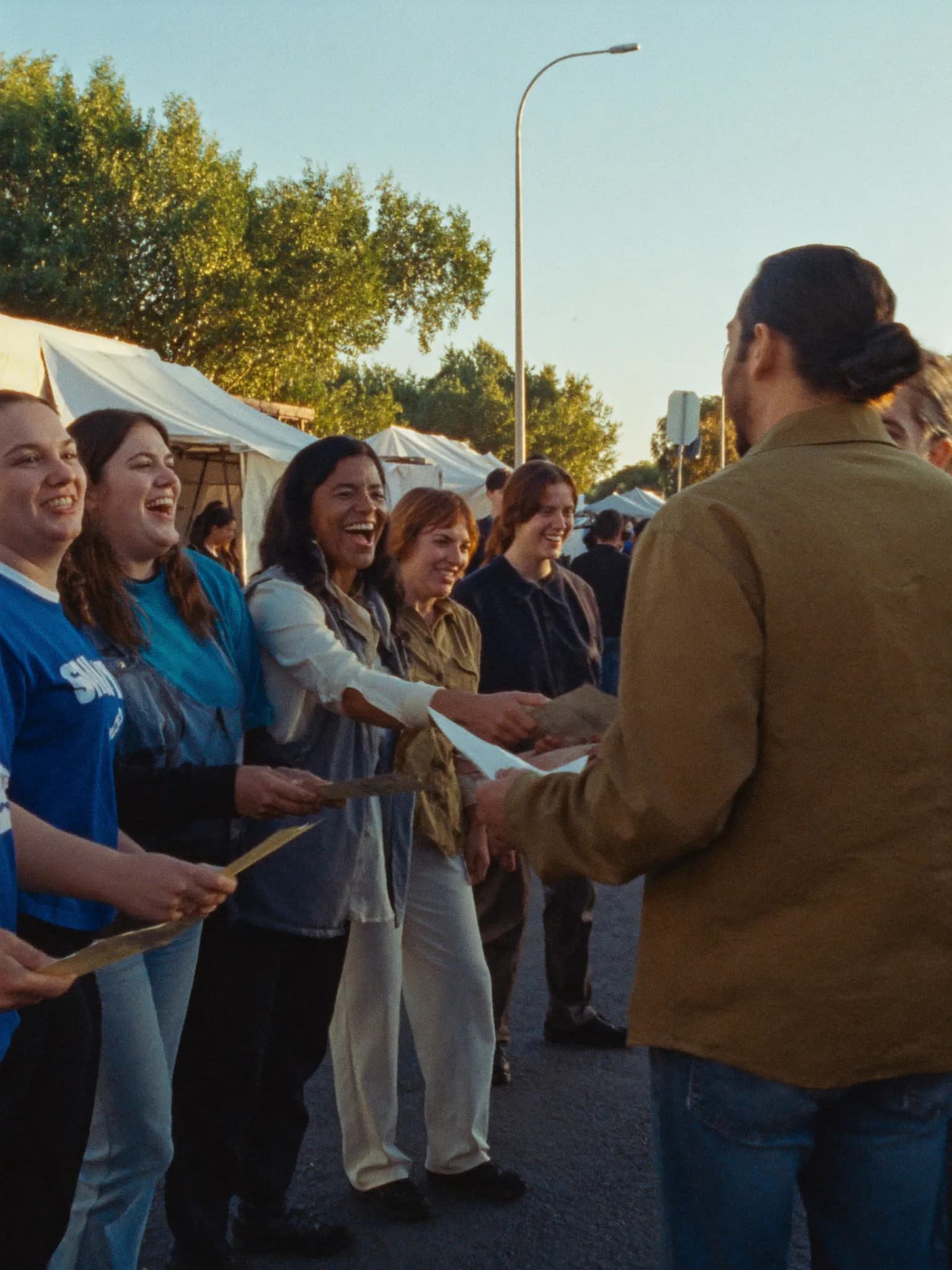 Volunteers laughing while greeting neighbors at a sunny street market
