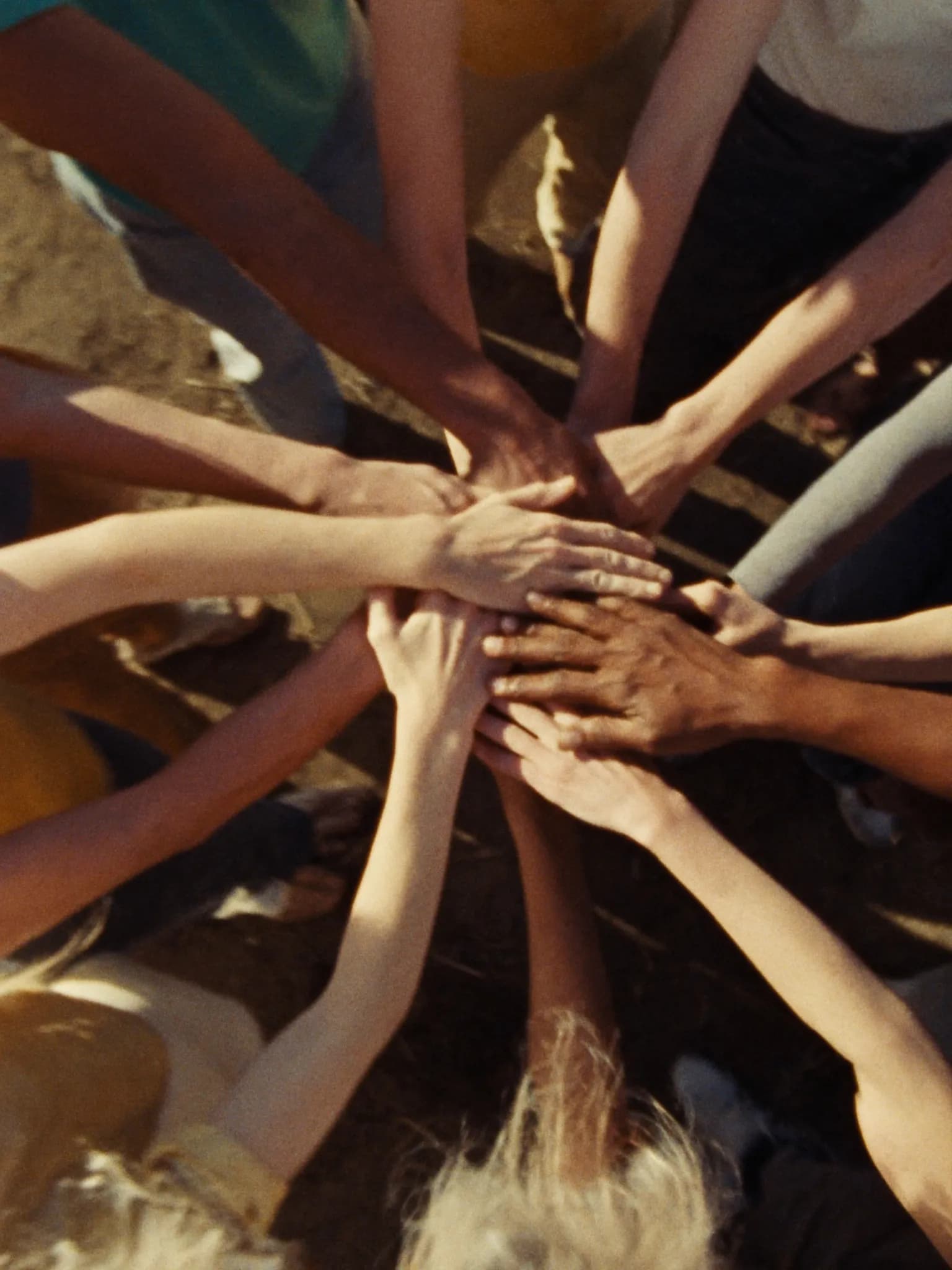 Many diverse hands joined together in the center of a circle of people in golden sunlight
