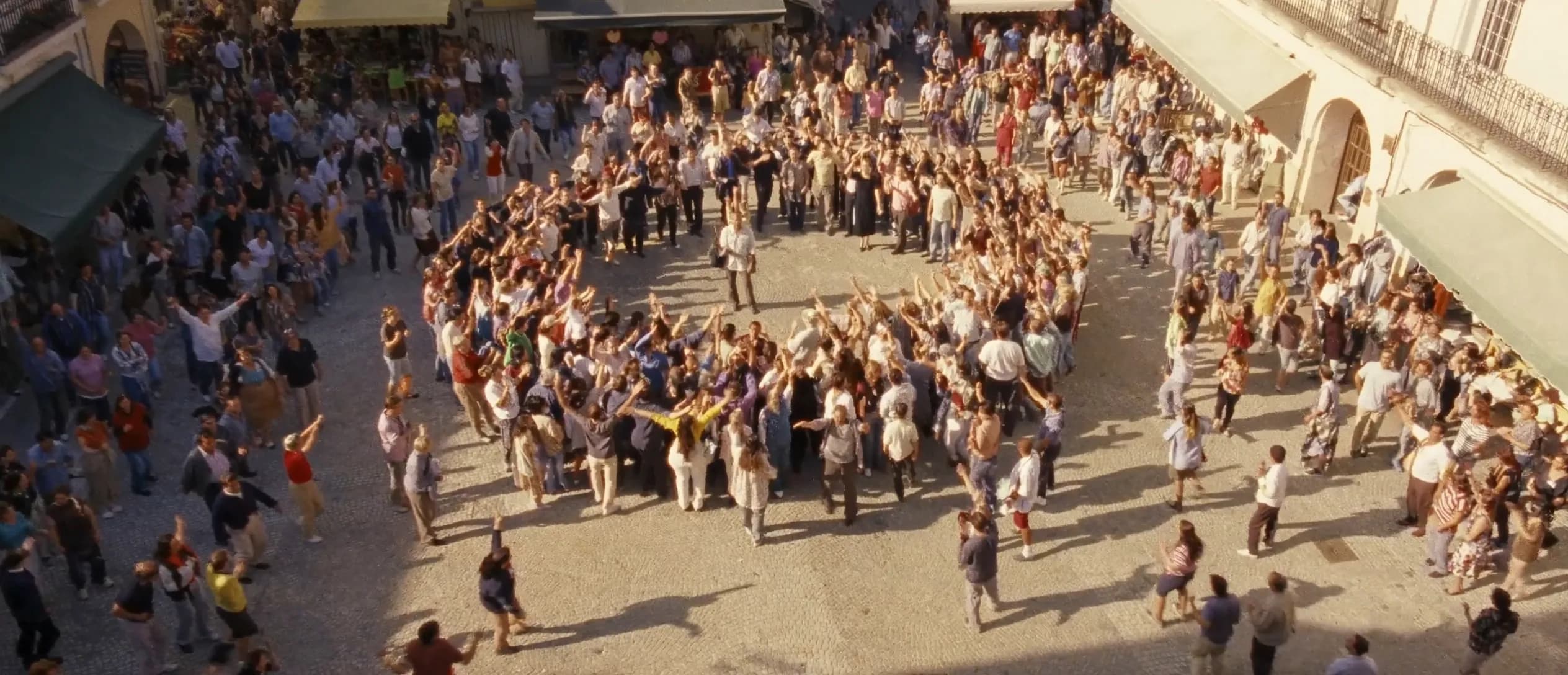 A sunlit town square where a joyful crowd gathers in a circle around a central point